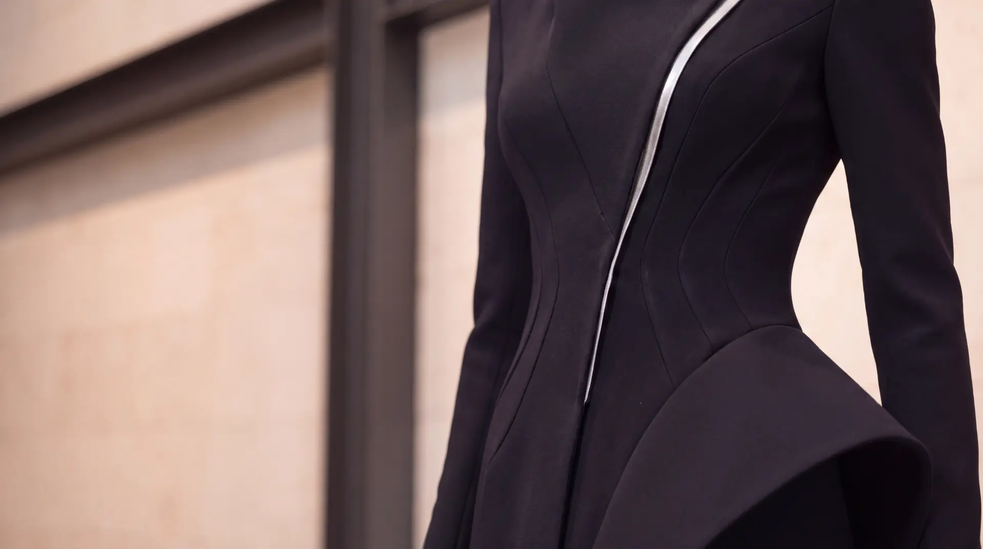 Close view of a black garment showing a curved silver seam and a sculptural folded hip panel