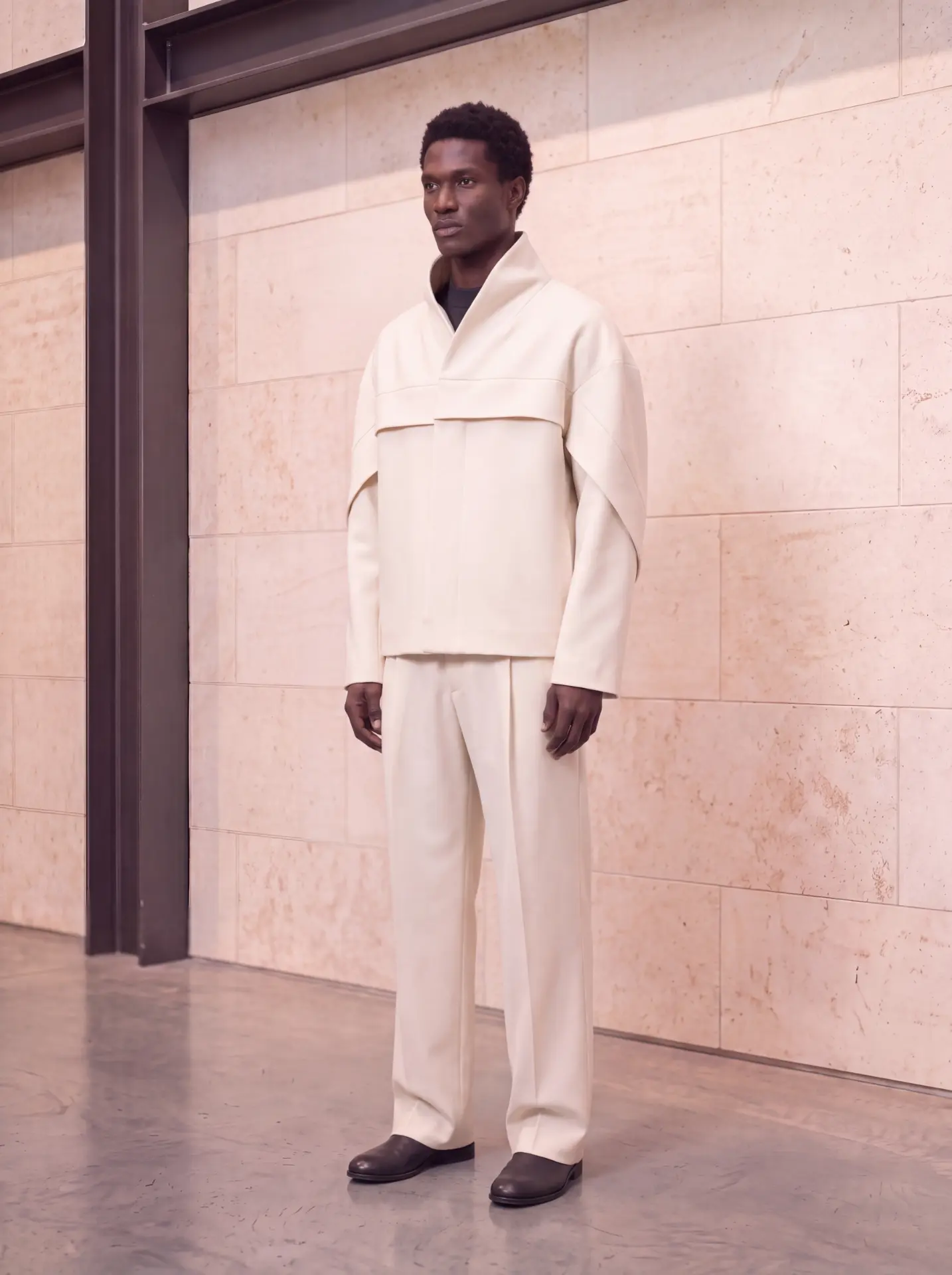 Ivory funnel-neck jacket with a horizontal chest fold, worn with ivory pleated trousers